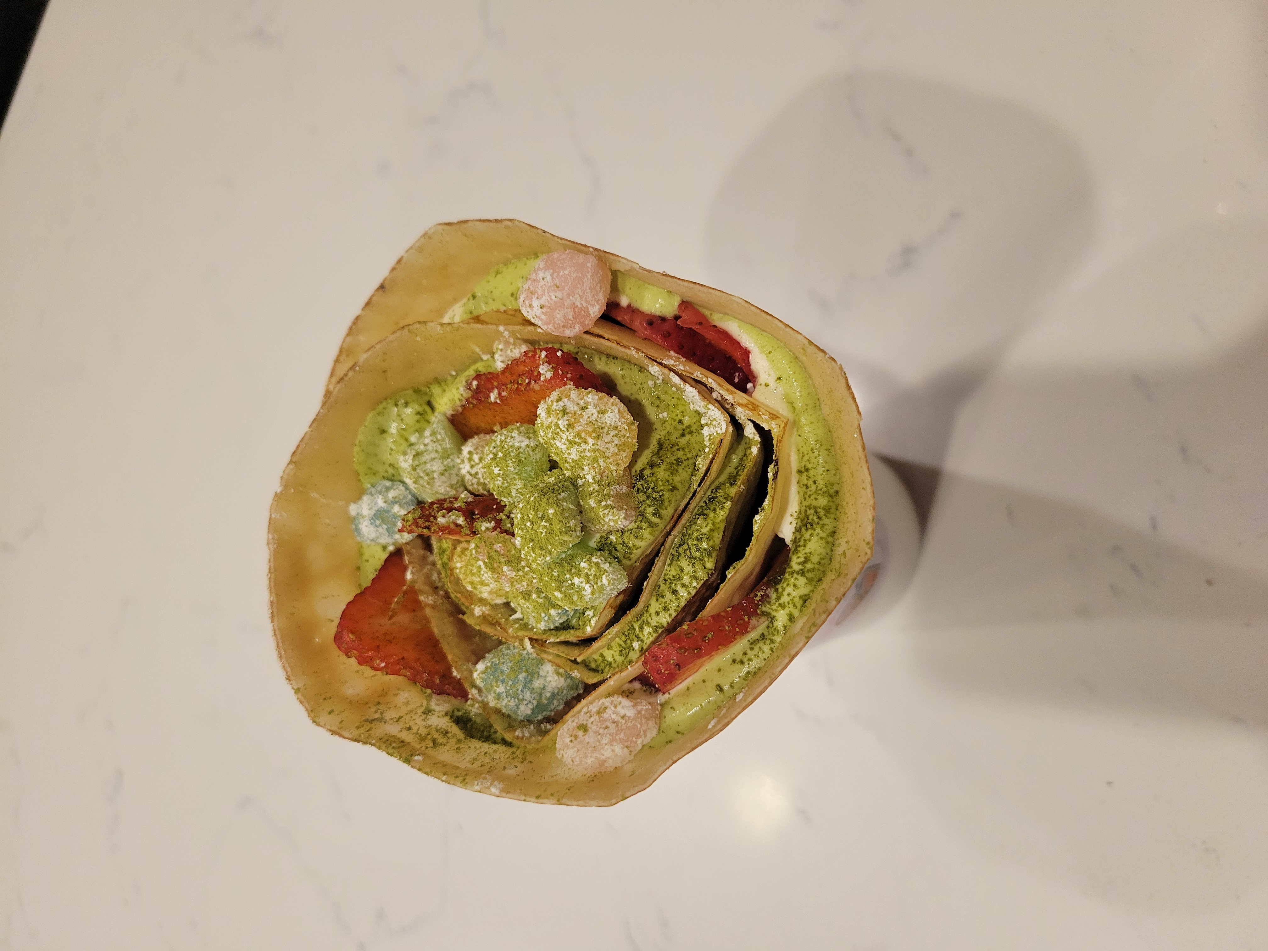 Strawberry with matcha filling, matcha powder and mochi crepe in a small cup.